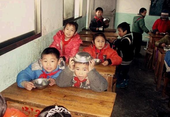 一群孩子迫不急待先拿着自己的碗勺，回到自己的座位等待老师开饭