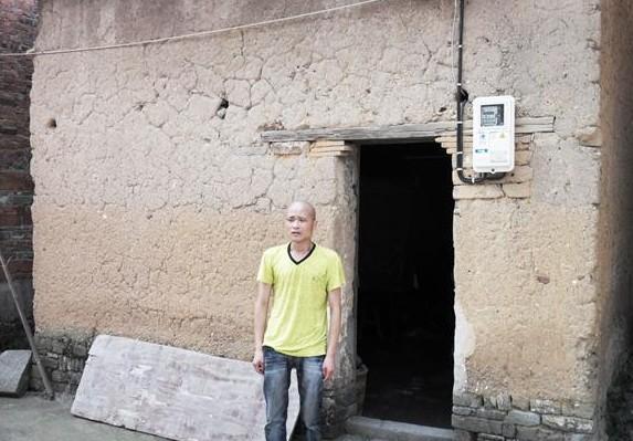 陈荣春站在家门口,居住老的泥土房子,墙壁多处裂缝,生活困难