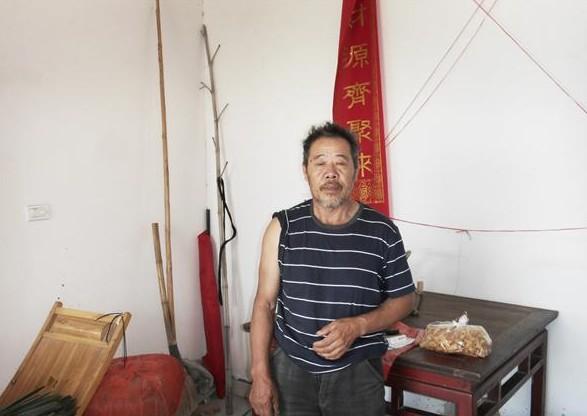 张贤生站在家里,家里用的家具都是老式的家具,房子是政府的危房改造工程时,政府补贴了一部分建造起来的。