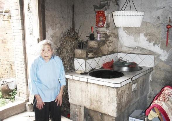 蒋爱招老人站在自己家的房子里面,土灶破旧,生活条件非常的差。