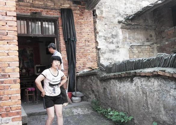 潘爱君站在家门口,他患有腰骨增生,腰椎突出,体弱多病走路比较吃力。