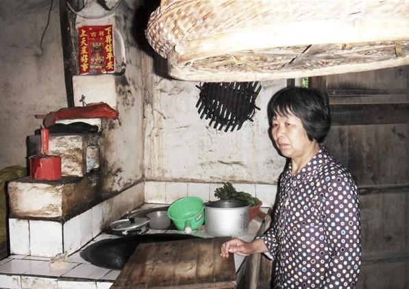 盛美芳站在家里,家里的土灶陈旧,没有像样的生活用品,靠她一个人维持家里生活,生活困难。