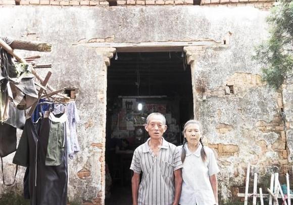 陈振民老人和妻子站在家门口,泥土房修修补补,非常无奈,生活十分困难。