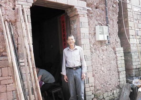 盛昌兴站在家门口,家居住的泥土房子,墙壁多处裂缝,下雨天漏雨。