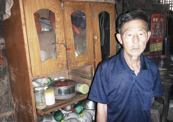 叶天金老人站在家里,家里用的生活的家具破旧,没有像样的生活用品。