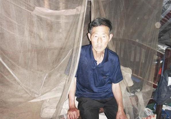 叶天金老人坐在自己的床上,生活家具陈旧,蚊帐都变色了,修修补补用了十来年