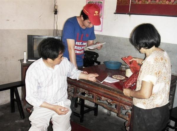 施乐会志愿者和乡村领导在蒋桂风家里了解情况,蒋桂风拿出相关证明。