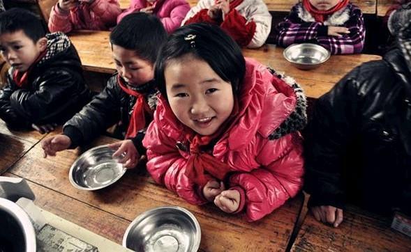 老师正在按顺序分发饭菜,后排的孩子都坐得特别端正,坐在前排的这个小姑娘,闻着饭香,早就迫不急待地站起来了