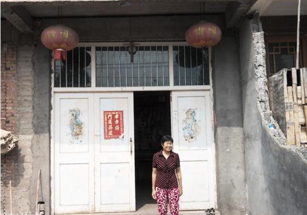 张玲凤站在家门口,早年建造的平房砖头瓦片盖两间两层平房子,比较的破旧,外墙壁补补修修,居住条件贫困。
