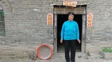 老人站在自家的老房子门口