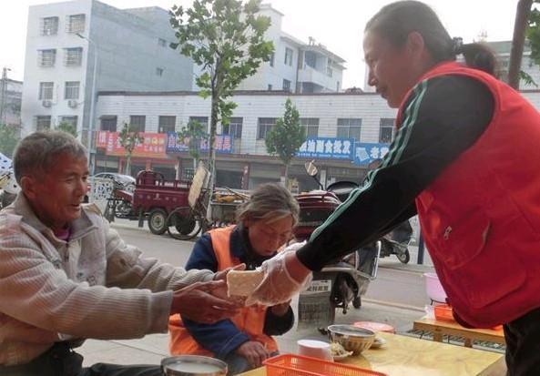 老人们行走不便,就让他们坐下来,志愿者将饭菜递到他们的手中